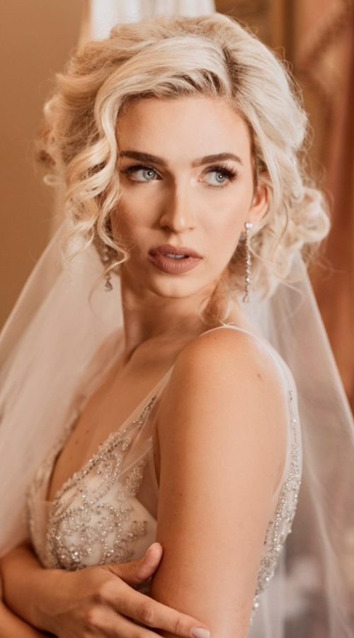 Bride in a veil with soft blonde curls and glowing makeup